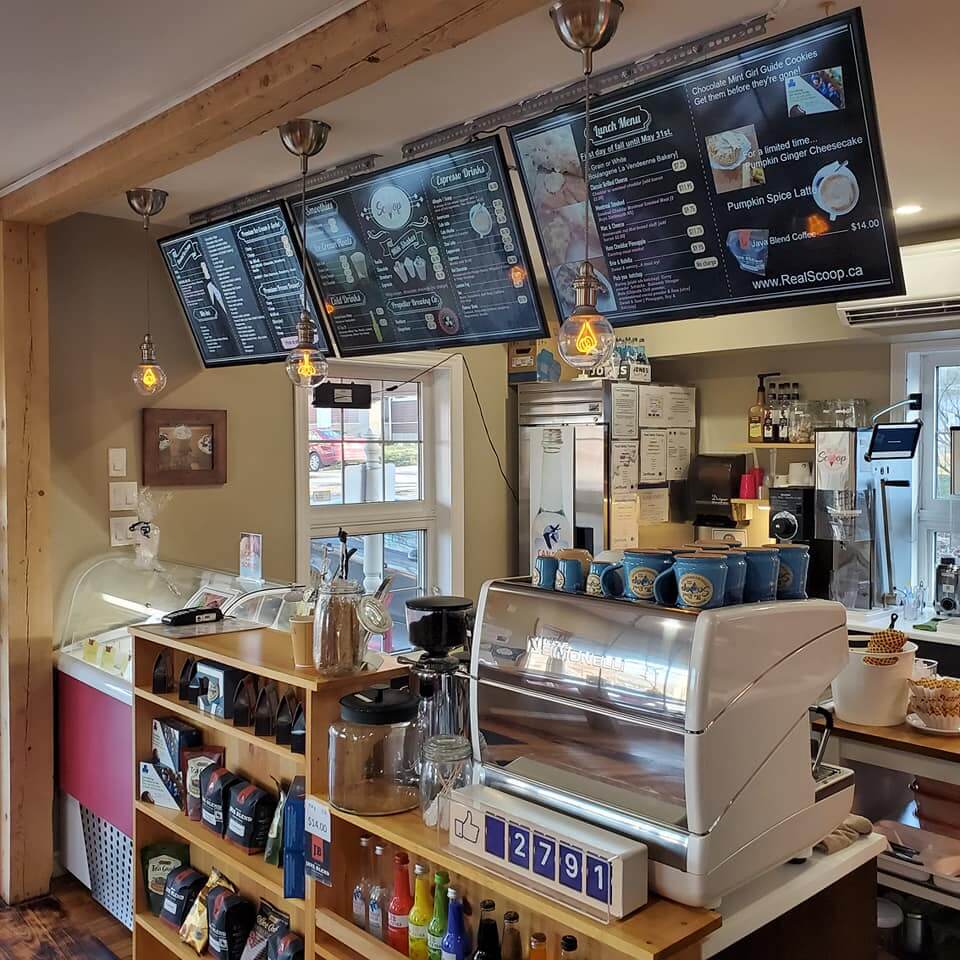Interior of The Real Scoop in Wolfville, Nova Scotia, showing espresso machine, ice cream counter, and menu boards