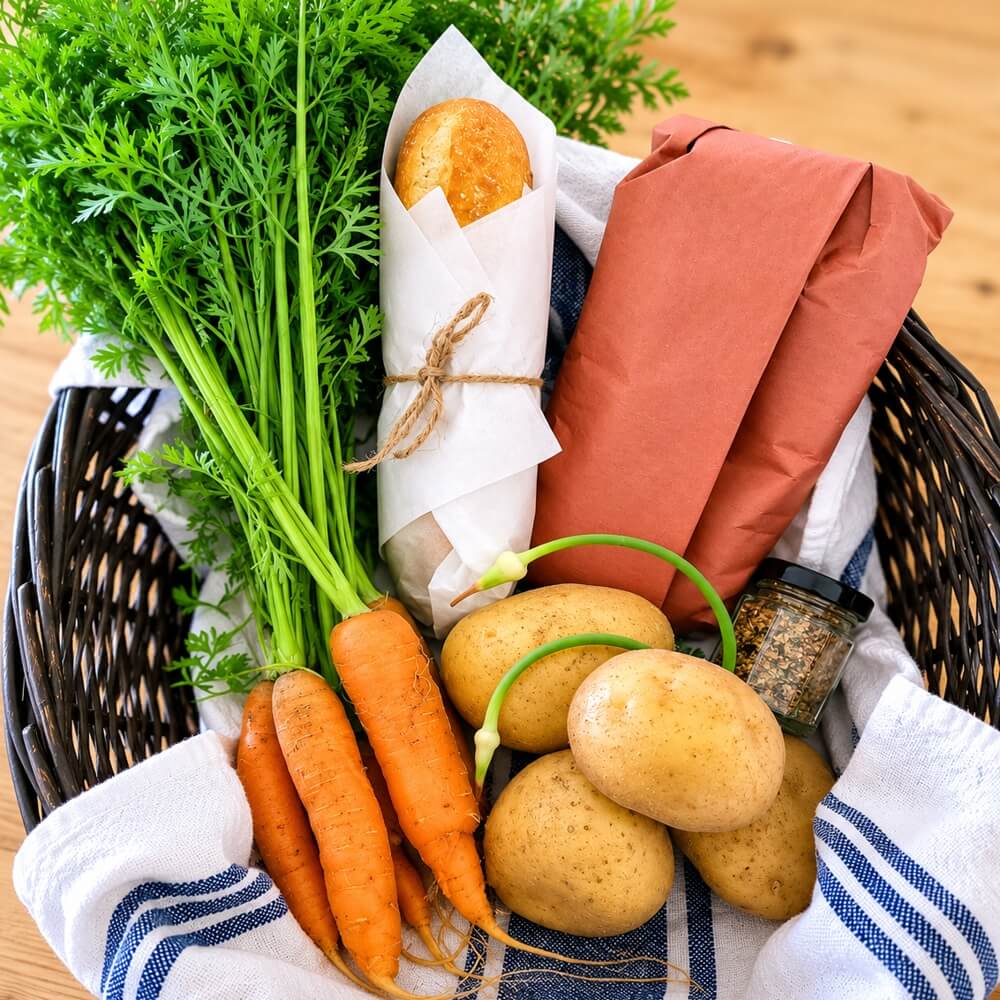Steak dinner basket with steaks, fresh vegetables, potatoes, baguette, chives, and seasoning ready for cooking